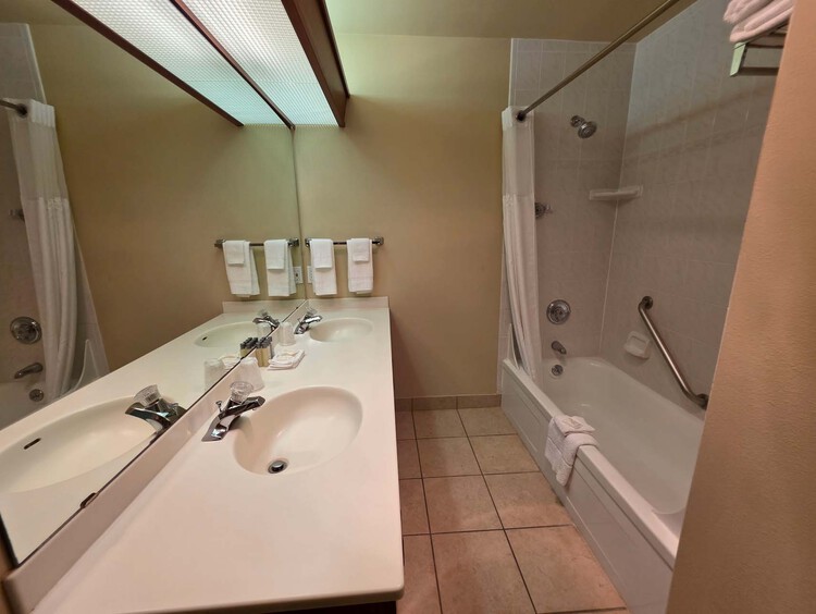 A bathroom with a double sink and a tub and shower combination with a grab bar